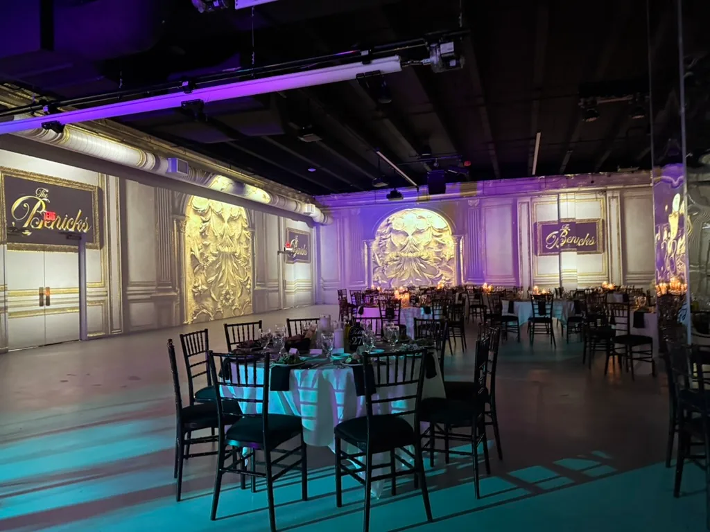 A ballroom set for dinner, its walls projected with gilded panels and the hosts' name.