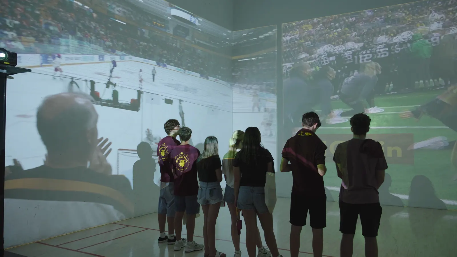 Students silhouetted against a projected hockey rink and a packed football stadium.