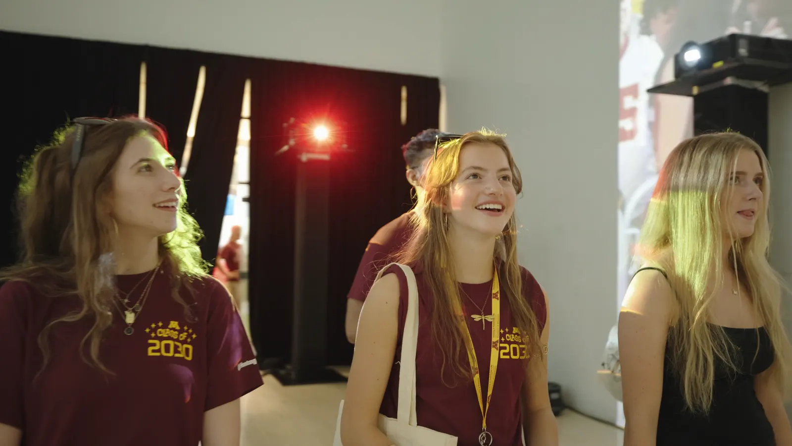 Three new students in Class of 2030 shirts looking up at the projected walls.